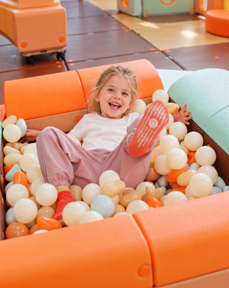 Smiling boy seated on Egoo Cosmotor mobile wheeled platform in front of modular playhouse cabin
